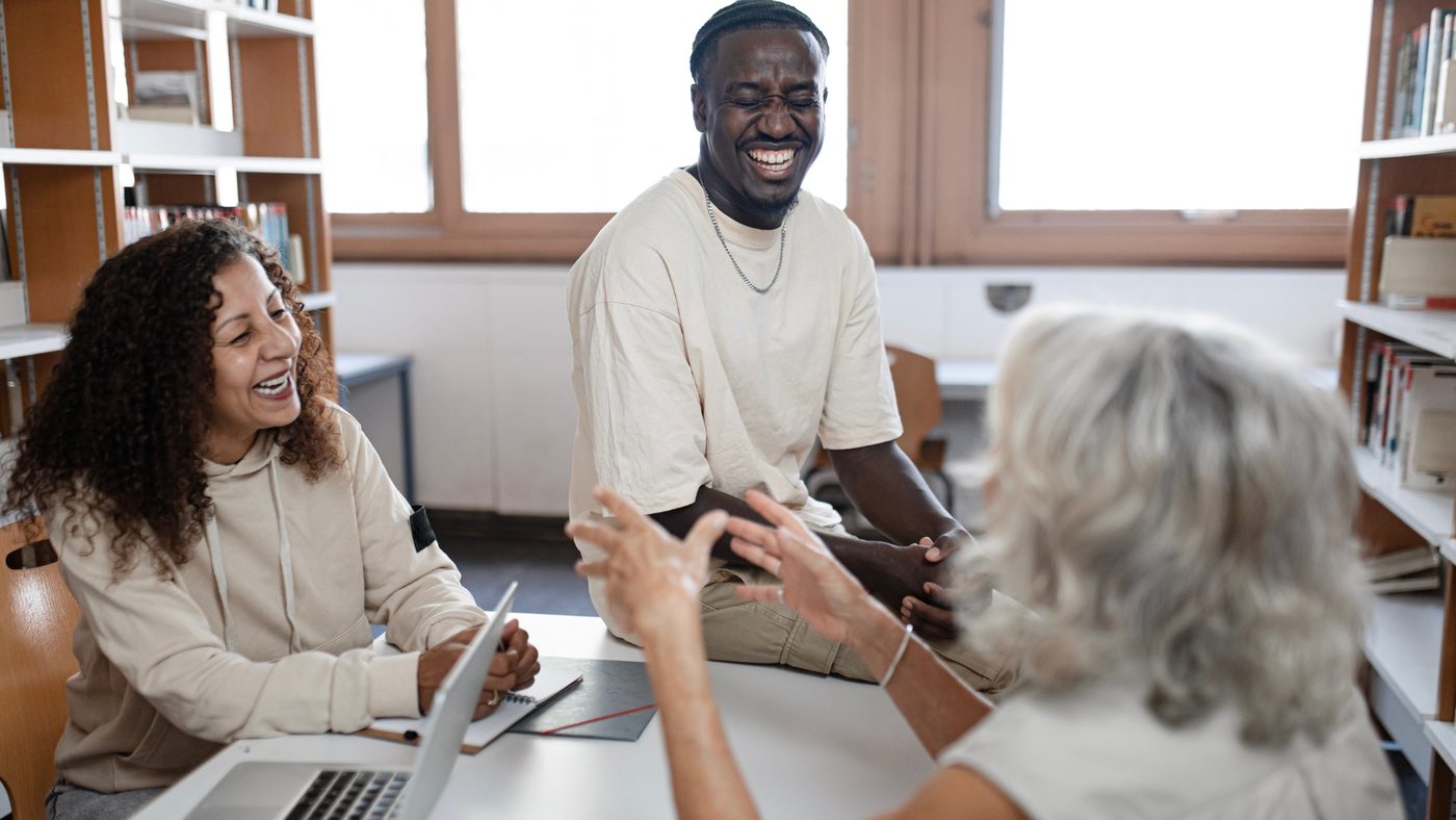 Three adults laughing together during a conversation in a library