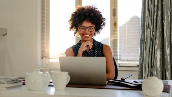 Smiling woman with curly hair and glasses seated at a laptop