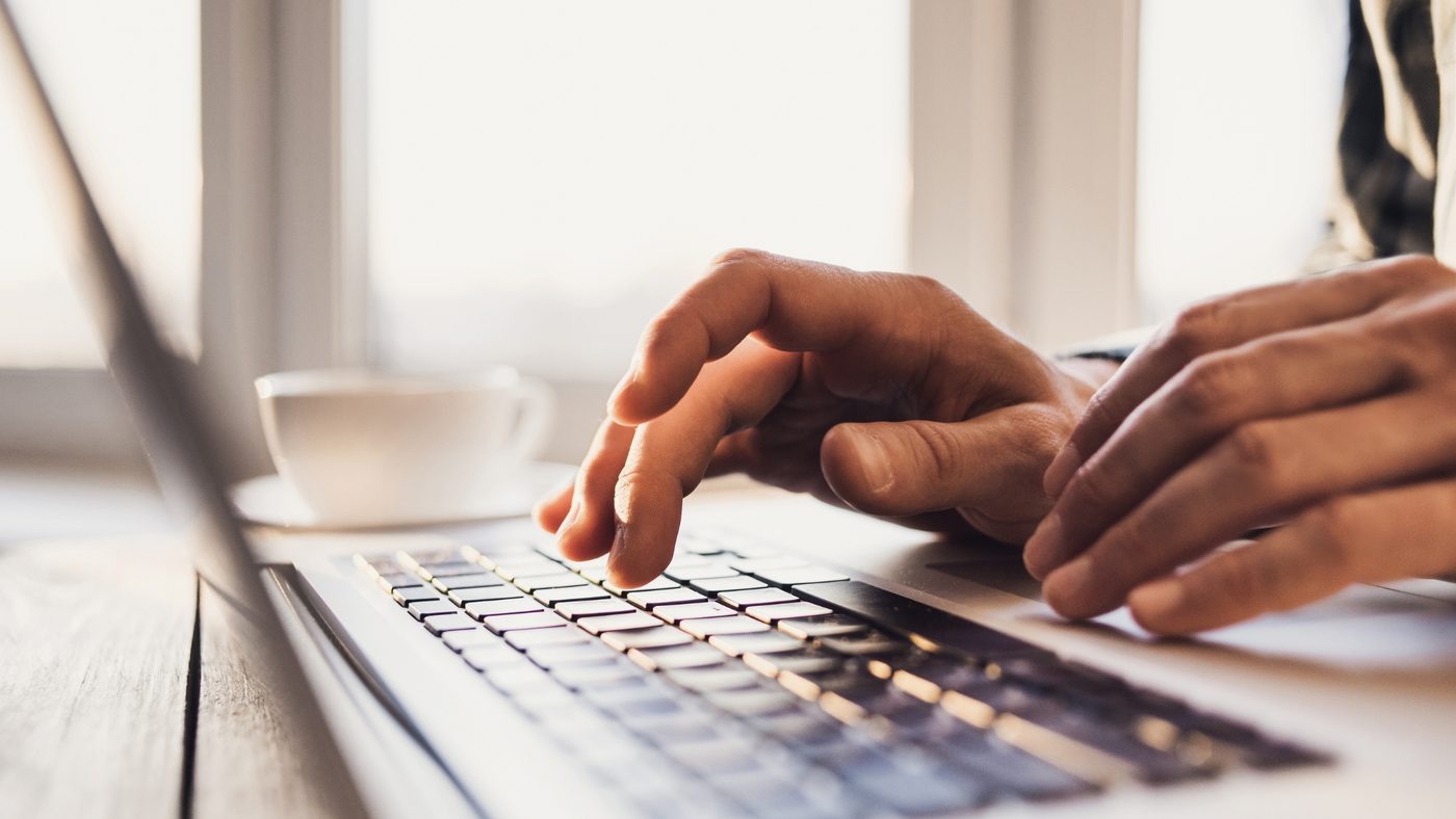 Close-up of hands typing on a laptop keyboard by a window